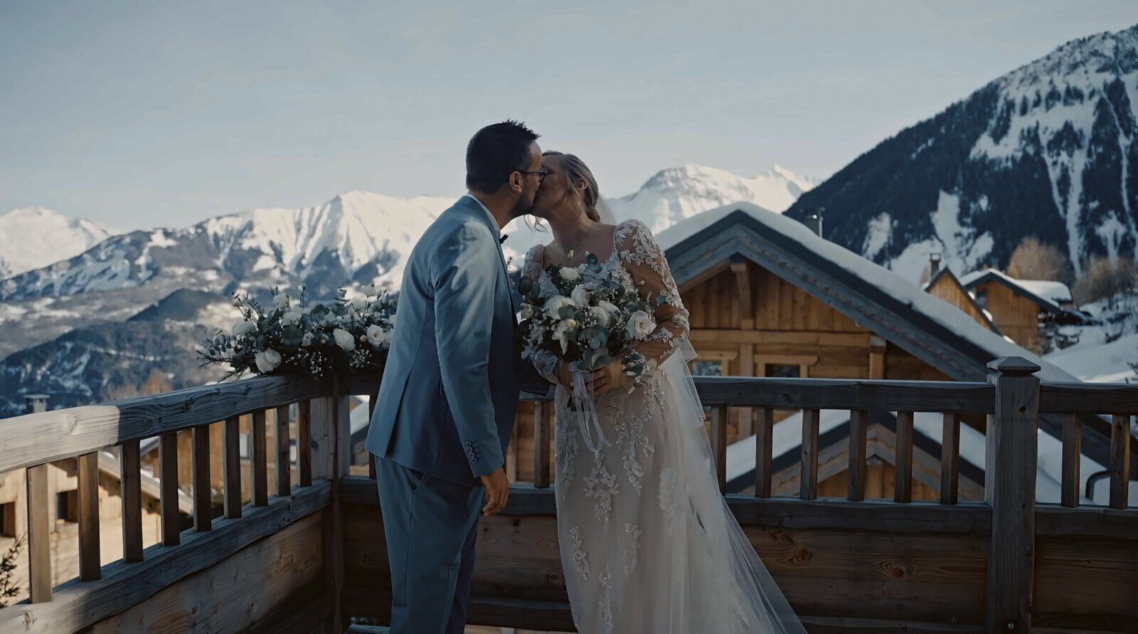 Baiser des mariés sur un balcon de chalet face aux sommets