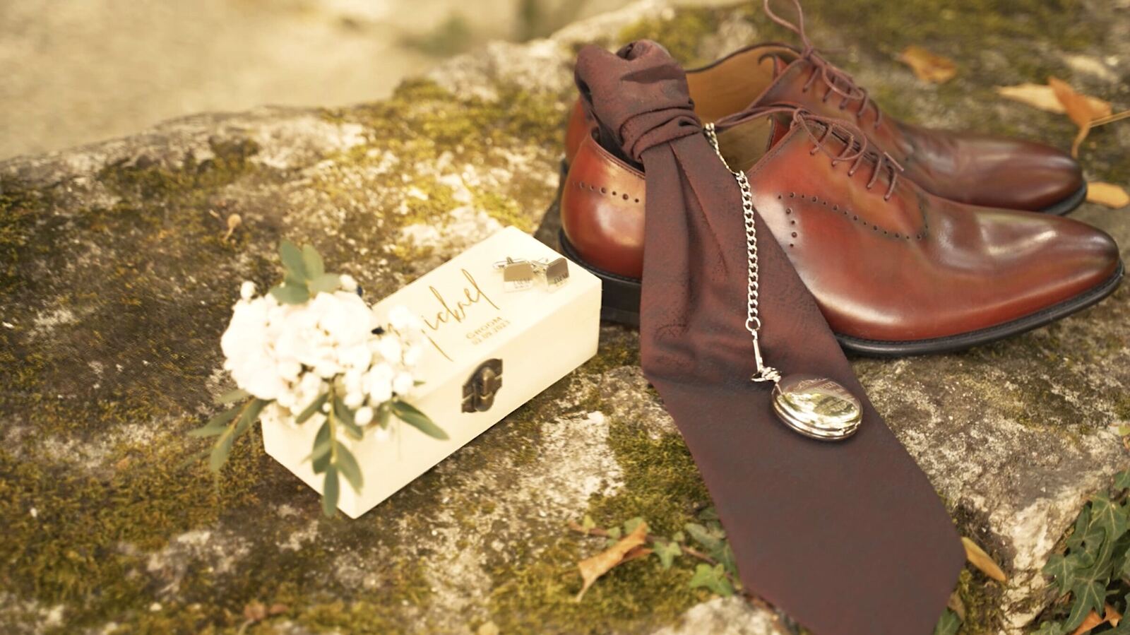 Chaussures, cravate et boîte à alliances posées sur un rocher